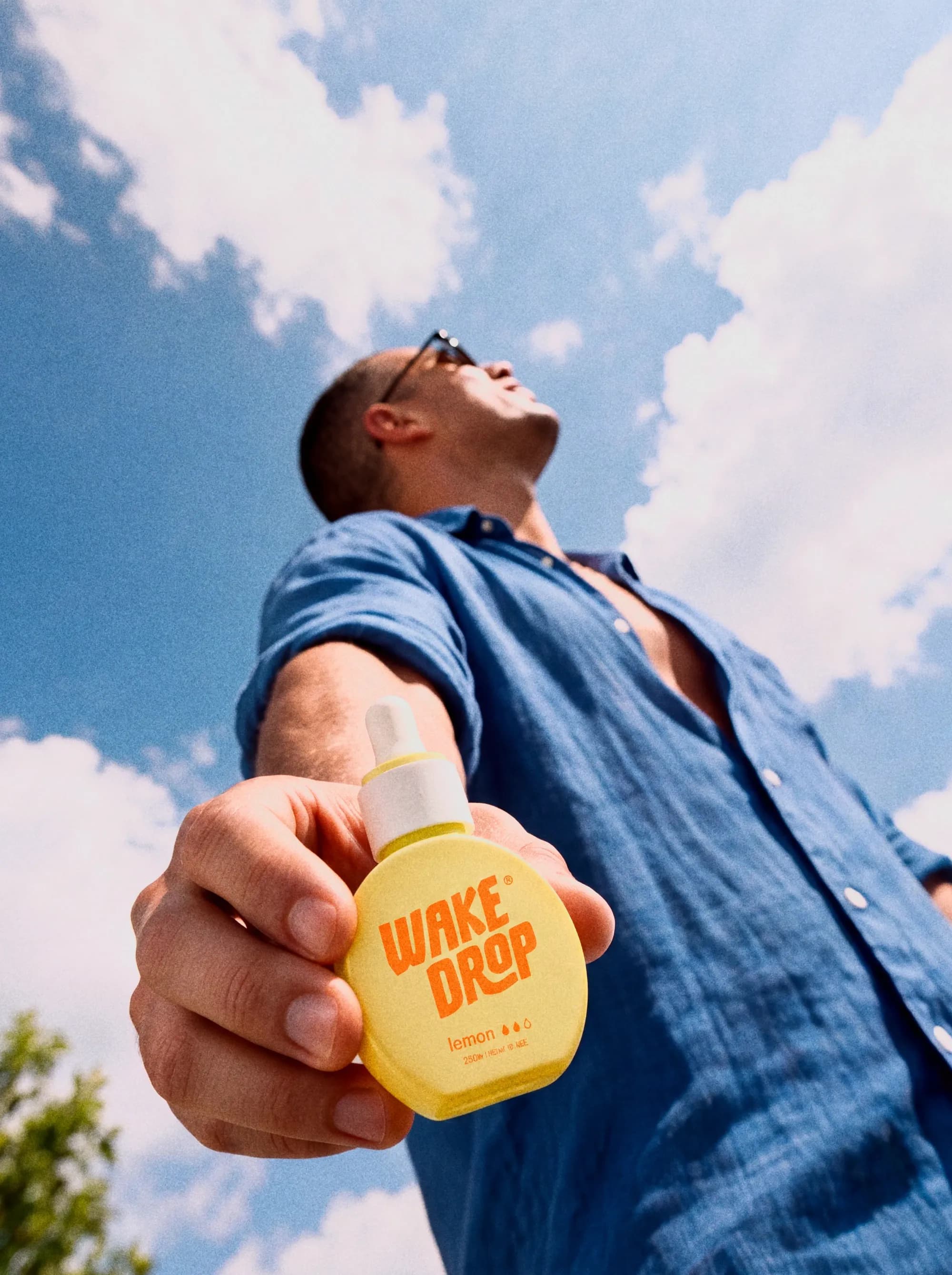 Man met een zonnebril en blauw overhemd houdt een flesje Wakedrop Lemon vast